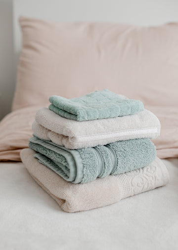 Stack of freshly laundered towels in sage and cream folded on clean bedding