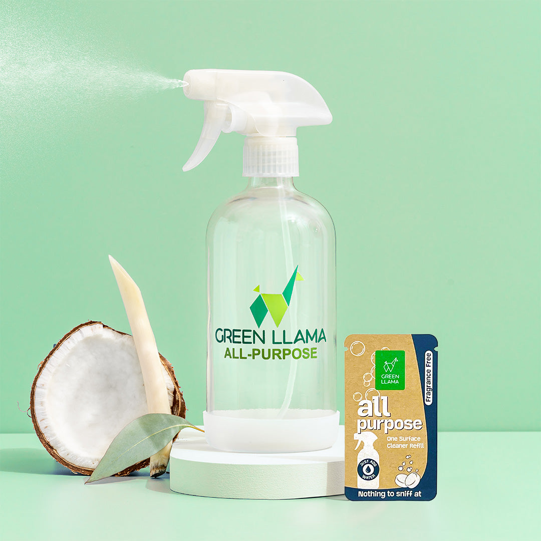 A packet of Green Llama Fragrance-Free All-Purpose Cleaning Refill stands upright beside a halved coconut against a green circle and a light green background.