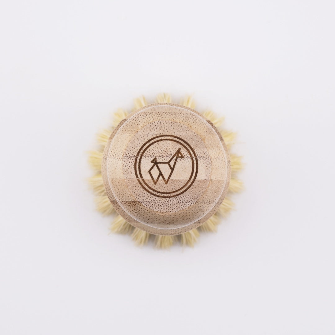 A round Sisal Dish Scrub Brush by Green Llama with light bristles and an engraved giraffe-in-circle logo, viewed from above on a plain white background.