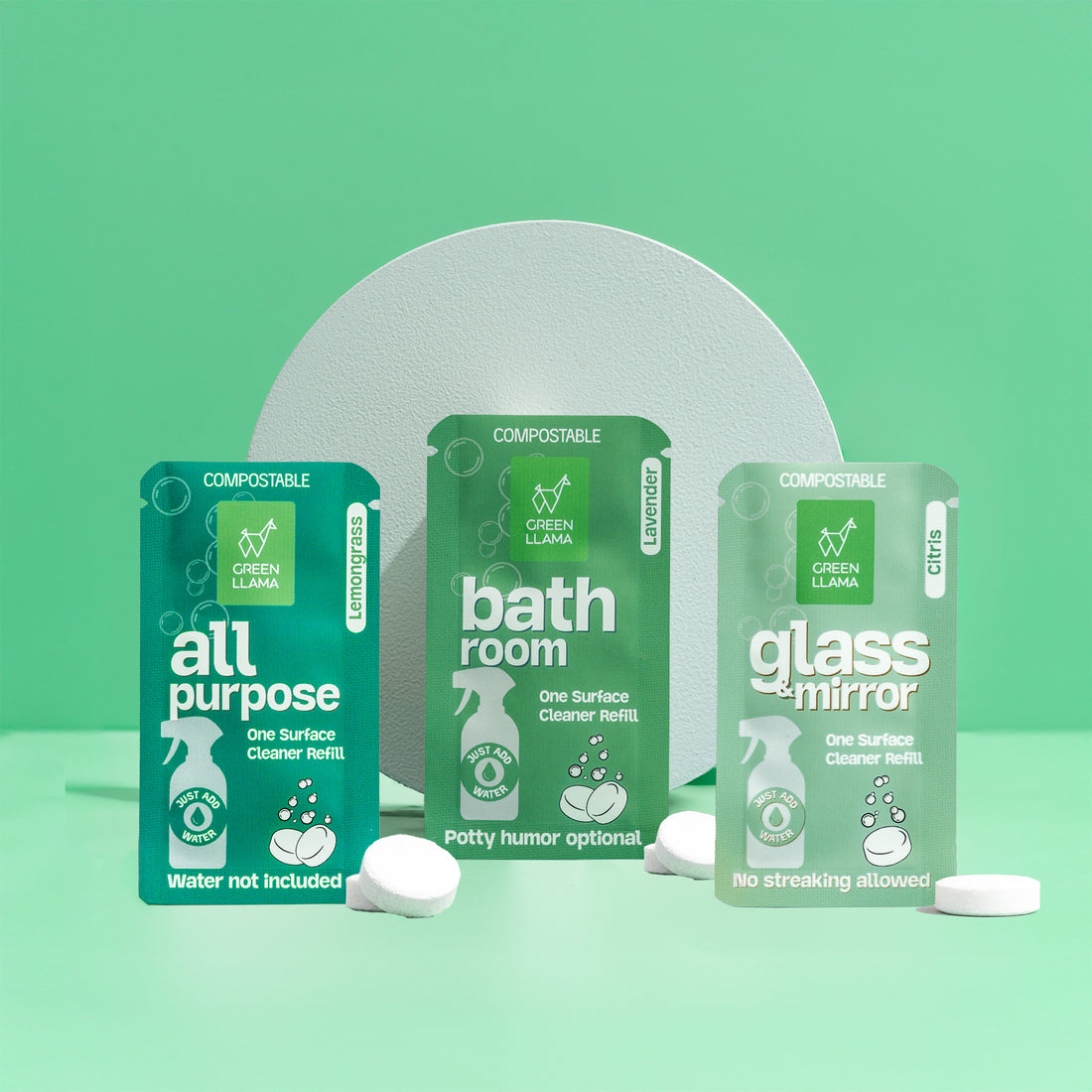 Green Llama’s Refill Cleaning Bundle features three green compostable packets—All Purpose, Bathroom, and Glass + Mirror—with eco-friendly cleaning tablets, displayed upright against a green background with a circular white backdrop.