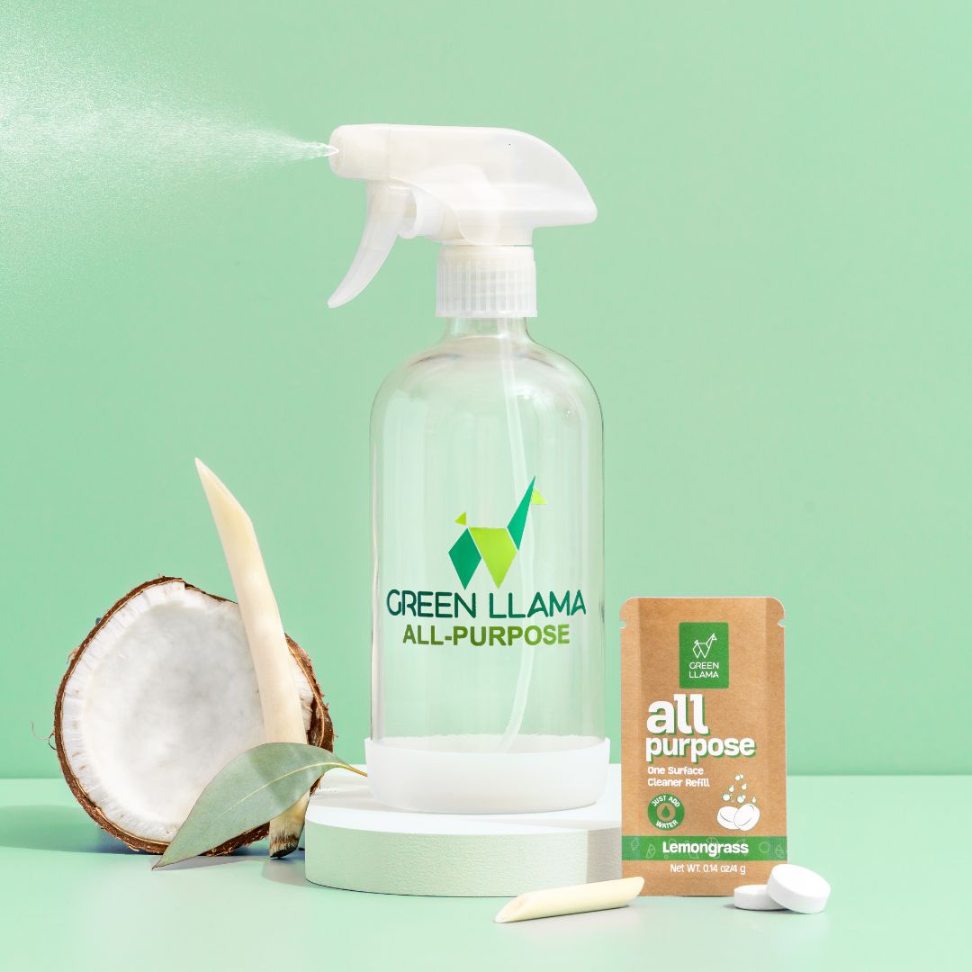 A Green Llama Digital Gift Card from Green Llama is displayed against a mint green background, accompanied by a coconut half, lemongrass stalk, green leaf, and brown eco-friendly cleaning packet.