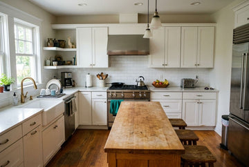 A bright, modern kitchen featuring white shaker-style cabinets, a central wooden island, a stainless steel gas range, a farmhouse sink, and hardwood floors.