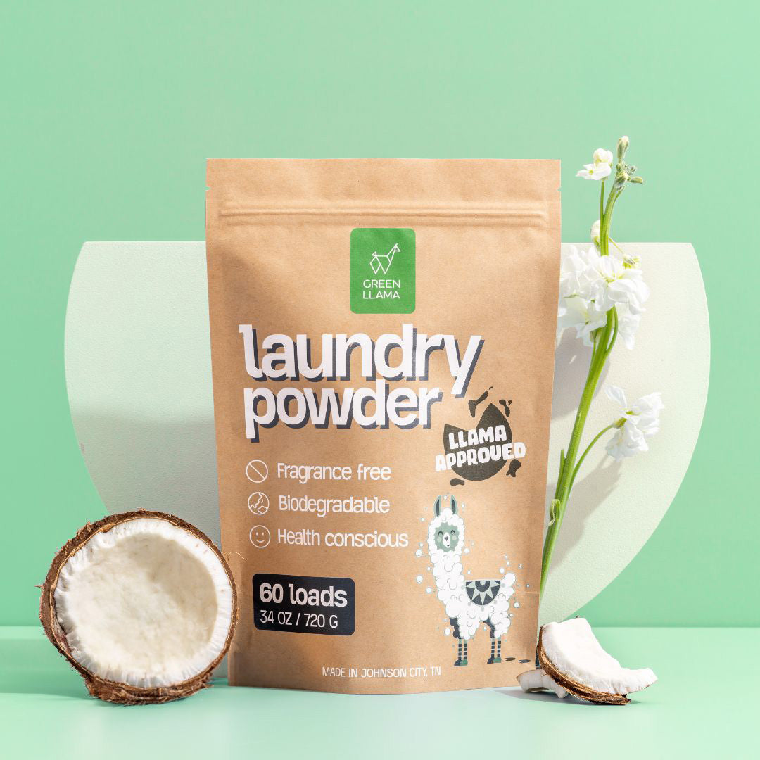 A brown bag from Green Llama’s The Ultimate Non-Toxic Home Bulk Bundle stands upright among coconut halves and white flowers on a pastel green background, showcasing its plant-powered, PVA-free laundry detergent formula.